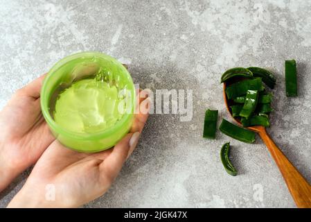 Mains de femmes avec du gel d'aloès et une cuillère avec des tranches de feuilles d'aloès sur fond gris. Faire des cosmétiques naturels à la maison. Banque D'Images