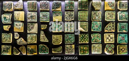 Petits carreaux de sol médiévaux avec des motifs géométriques – cercles, losanges, lignes de grille – sont disposés densément dans une vitrine du Palais des Papes d'Avignon, France. Banque D'Images
