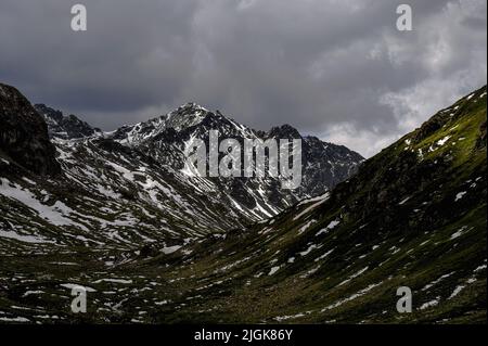 Sous le nuage gris, la neige strie les pentes des Alpes rhétiennes en juillet dans cette vue de la route reliant Davos et Susch via le 2 383 m / 7 818 ft Fluela Pass dans le canton de Graubunden, Suisse. Banque D'Images