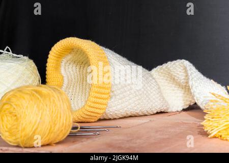 le chapeau d'elf de bébé crocheted sur des planches en bois et un fond noir, à côté de lui deux rouleaux de fil jaune et blanc, des matériaux pour commencer le crocheting. concept Banque D'Images