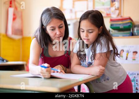 Une jeune femme enseignante aide un élève de l'école primaire en classe à apprendre une leçon. Concept d'éducation et de développement des enfants. Banque D'Images