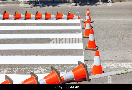 Les marquages routiers rayés récemment peints d'un passage pour piétons de l'autre côté de la route sont clôturés avec des cônes de circulation lors d'une journée ensoleillée d'été. Copier l'espace. Banque D'Images