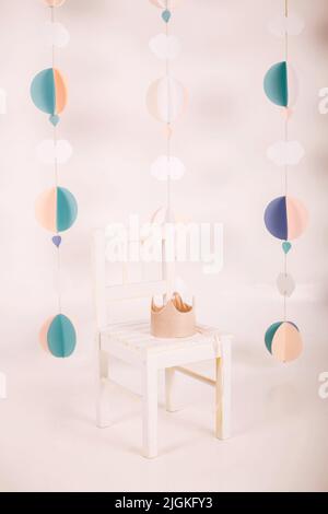 La couronne rose repose sur une chaise dans la salle rose. Concept ou carte postale de l'intérieur des enfants. Maison confortable. Guirlande de papier ronde. Bricolage papier artisanal. Origami Banque D'Images