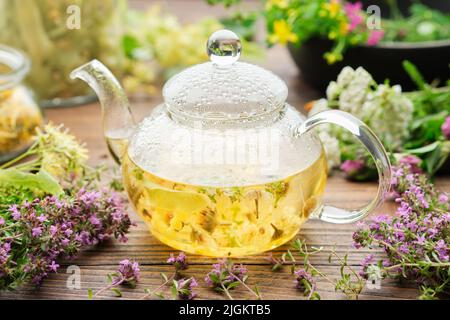 Thé en verre bouilloire de thé à base de plantes saines, thym, fleur de tilleul, millepertuis, yarrow, camomille, calendula herbes médicinales sur table en bois. Alternatif Banque D'Images