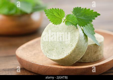 Morceaux de shampooing solides d'ortie ou barres de savon biologique naturel maison, feuilles d'ortie vertes fraîches. Mise au point sélective. Banque D'Images