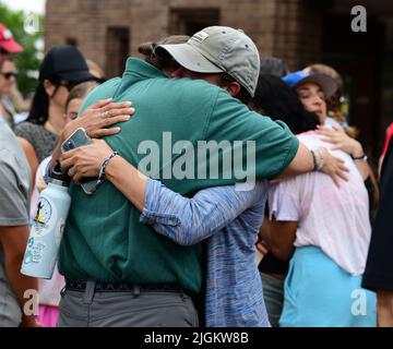 Highland Park, Illinois, États-Unis. 11th juillet 2022. Les gens se réconfortent les uns les autres et se rassemblent dans le centre-ville de Highland Park, Illinois, près de la scène du défilé du 4th juillet de fusillade de masse qui a tué sept personnes et blessé plusieurs douzaines d'autres. Des minutes de silence ont été observées là-bas et dans les communautés voisines à 10 h 14, heure de la fusillade. Sept chaises commémorant les victimes sont entourées d'hommages floraux. (Image de crédit : © Mark Hertzberg/ZUMA Press Wire) Banque D'Images