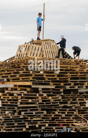 Larne, Irlande du Nord, Royaume-Uni, Royaume-Uni. 11th juillet 2022 - les enfants grimpent sur la petite pile de feu de joie le 11th juillet, traditionnellement quand les protestants d'Irlande du Nord allument des feux de joie. Banque D'Images