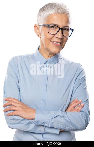 Belle souriante femme d'affaires senior avec des lunettes et une chemise bleue avec des cheveux blancs courts gris et des lunettes posant. Isolé sur blanc Banque D'Images