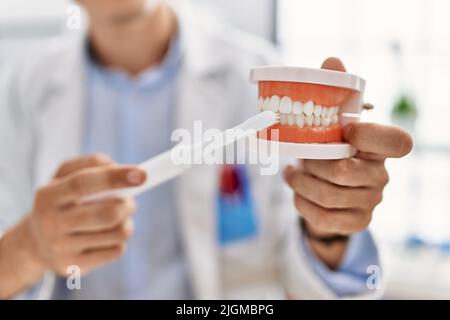 Jeune homme caucasien portant une prothèse dentaire uniforme de dentiste utilisant une brosse à dents à la clinique Banque D'Images