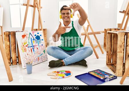 Jeune homme hispanique dans un studio d'art souriant faisant cadre avec les mains et les doigts avec le visage heureux. Créativité et concept de photographie. Banque D'Images