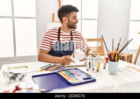 Jeune artiste arabe homme souriant dessin heureux au studio d'art. Banque D'Images