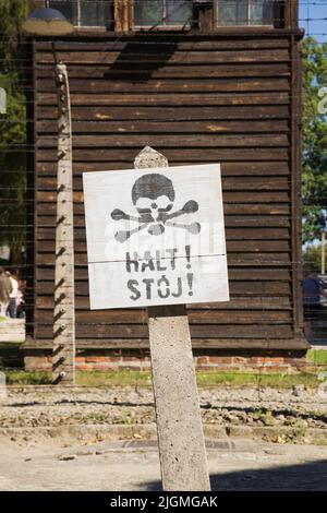 Panneau d'avertissement et clôture de barbelés devant une tour de garde à l'intérieur de l'ancien camp de concentration nazi d'Auschwitz I, Auschwitz, Pologne. Banque D'Images