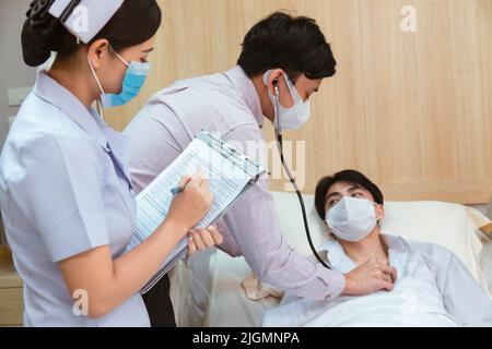 homme asiatique patient allongé dans le lit pendant que le médecin vérifie le rythme cardiaque par stéthoscope et femme infirmière écrivant la liste de contrôle de santé à l'hôpital. soins de santé et ho Banque D'Images