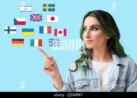 Jolie jeune femme et différents drapeaux sur fond bleu clair. Étudier des langues étrangères Banque D'Images