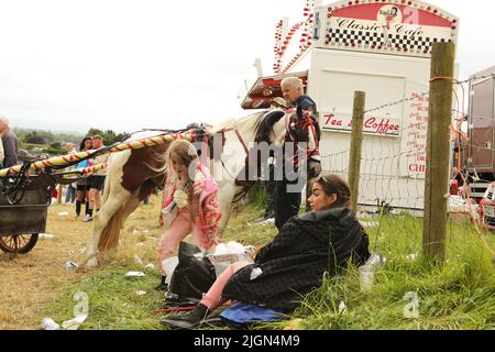 Une mère et un enfant assis sur l'herbe devant un homme debout avec un poney coloré et un piège. Appleby Horse Fair, Appleby à Westmorland, Cumbria Banque D'Images