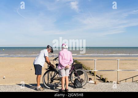 Homme et femme cyclistes se préparer à quitter la plage de sable pour la maison après une journée chaude et belle sur la plage Kent Angleterre Royaume-Uni Banque D'Images