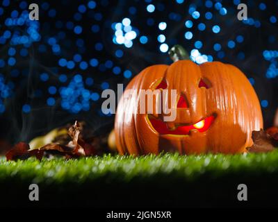 Une citrouille orange avec un sourire illuminé de l'intérieur, des fruits et des cônes sur l'herbe verte contre un ciel étoilé bleu. Arrière-plan de Halloween. Publicité, Banque D'Images