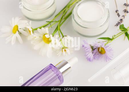 Bocaux à crèmes organiques, bouteille de sérum et fleurs sauvages sur fond blanc. Concept de beauté sauvage et de cosmétiques naturels basés sur un Banque D'Images