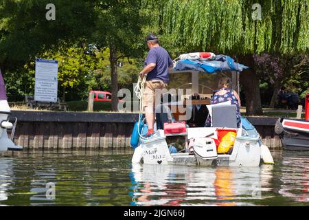 Vue arrière d'un bateau à moteur avec deux personnes naviguant vers des amarres sur la rivière Ouse, un jour où les températures ont augmenté à 30. Ely, Cambridgeshire, Royaume-Uni Banque D'Images