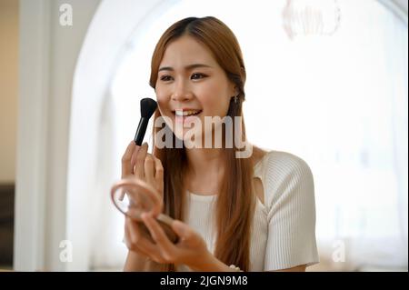 Jolie et attrayante jeune femme asiatique faisant son maquillage, appliquant un beau rougissement rose sur. Beauté et mode Banque D'Images