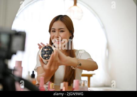 Belle et talentueuse jeune femme asiatique blogueur ou influenceur de beauté est en direct-streaming pour examiner son produit cosmétique, montrant sa poudre de presse à un Banque D'Images