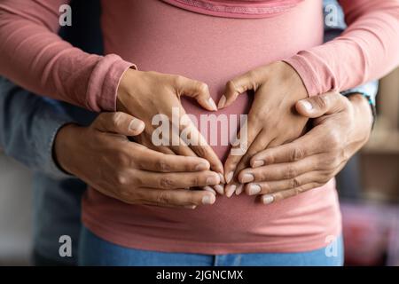 Couple musulman noir faisant le coeur sur le ventre enceinte avec leurs mains Banque D'Images