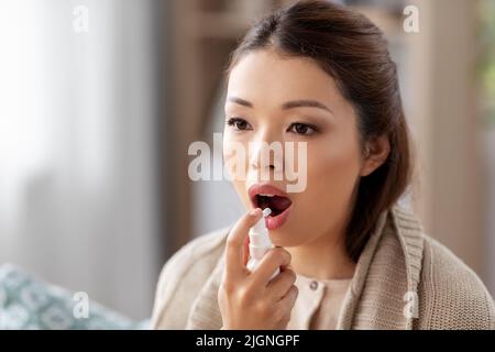 femme asiatique malade utilisant la médecine par pulvérisation orale à la maison Banque D'Images