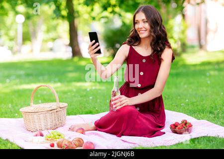 bonne femme avec un smartphone et un verre au parc Banque D'Images