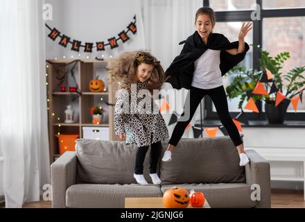 les filles en costumes d'halloween sautant sur le canapé Banque D'Images