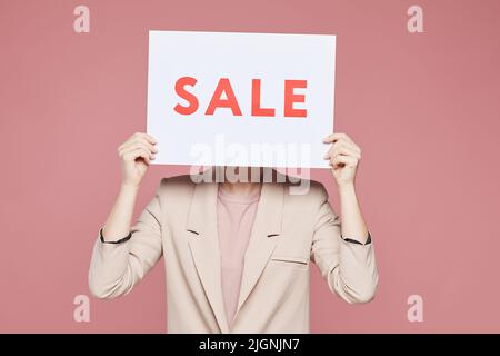 Femme dans une veste élégante debout sur fond rose et cache face derrière la bannière solde Banque D'Images