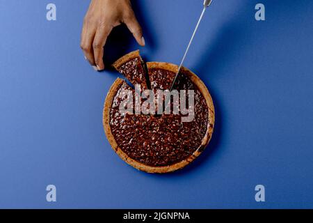 Composition des mains de l'homme biracial coupant une tarte avec couteau sur fond bleu Banque D'Images