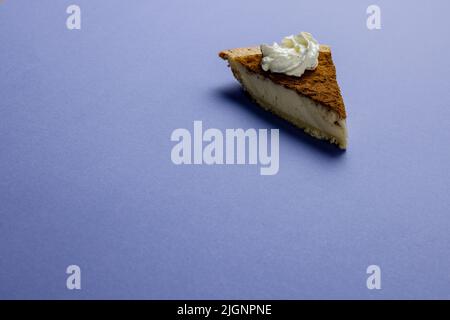 Composition d'un morceau de tarte à la citrouille avec de la crème fouettée sur fond bleu Banque D'Images