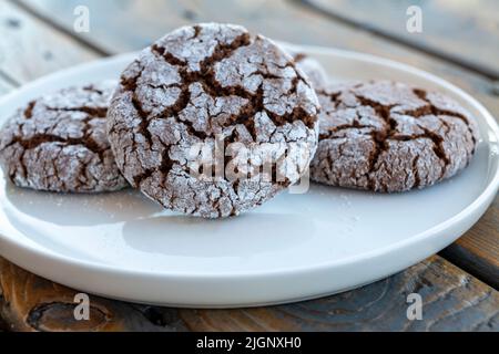 Biscuits faits maison aux amandes au cacao saupoudrés de sucre en poudre sur une assiette sur fond de bois Banque D'Images