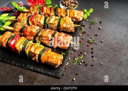 Morceaux de kebab grillés avec légumes sur brochettes sur un tableau noir en céramique sur fond sombre avec feuilles de basilic frais.morceaux de viande de poulet grillé Banque D'Images