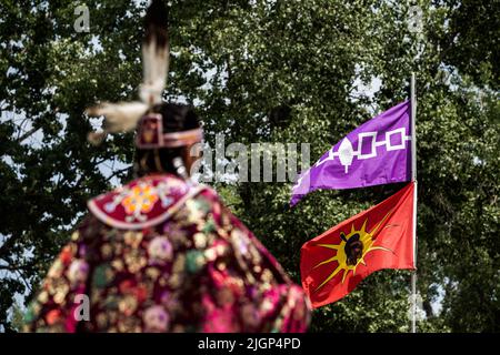 Une participante à la pow-wow attend son tour devant le drapeau du guerrier Mohawk et le drapeau de la Confédération iroquois pendant le festival. Banque D'Images