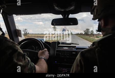 Personnes en uniforme de camouflage dans une voiture sur la route parmi les champs de blé en feu Banque D'Images