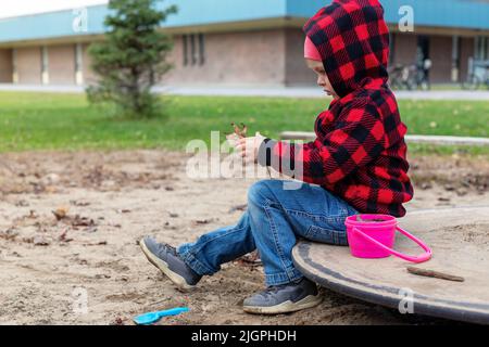 Petit enfant jouant avec du sable et des jouets à l'extérieur dans la cour d'école le jour ensoleillé. Petite fille assise à l'aire de jeux Banque D'Images