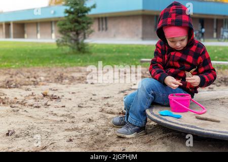 Petit enfant jouant avec du sable et des jouets à l'extérieur dans la cour d'école le jour ensoleillé. Petite fille assise à l'aire de jeux Banque D'Images