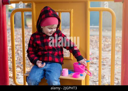 Petit enfant souriant heureux jouant avec du sable et des jouets à l'extérieur dans la cour de l'école. Petite fille assise à l'aire de jeux Banque D'Images