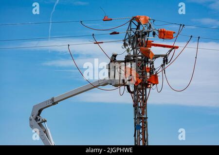 Un travailleur méconnaissable dans un panier de relevage hydraulique effectuant des travaux d'entretien sur une ligne électrique Banque D'Images