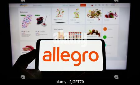 Personne tenant un smartphone avec le logo de la société polonaise d'e-commerce Allegro.pl SP. z O. O. sur l'écran devant le site Web. Mise au point sur l'affichage du téléphone. Banque D'Images