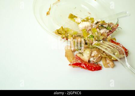 Vieille salade déversée d'une assiette en plastique sur une table blanche, gros plan Banque D'Images