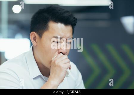 Photo portrait en gros plan d'un asiatique dans une chemise, un homme d'affaires malade tousse dans un tissu. Banque D'Images