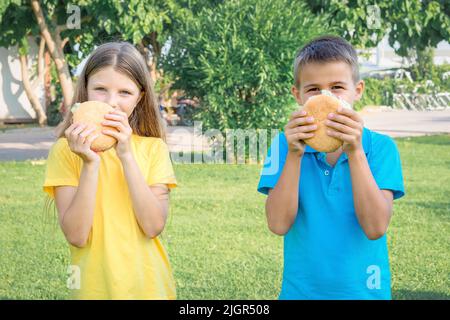 Les écoliers mangent des hamburgers dans le parc. Déjeuner après l'école. Banque D'Images