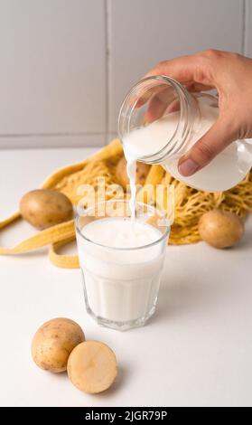 Lait de pomme de terre versé dans le verre sur fond blanc de table Banque D'Images