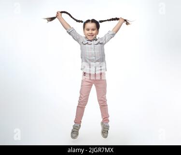 charmante petite fille avec des picots tressés sautant dans le studio sur un fond blanc. Banque D'Images