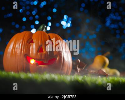 Citrouille d'Halloween avec un sourire, illuminée de l'intérieur avec une bougie sur une pelouse verte contre un ciel étoilé bleu. Bannière, publicité, affiche, dans Banque D'Images