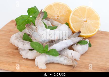 Crevettes crues congelées pelées sur une planche à découper en bois avec des herbes et du citron. Banque D'Images