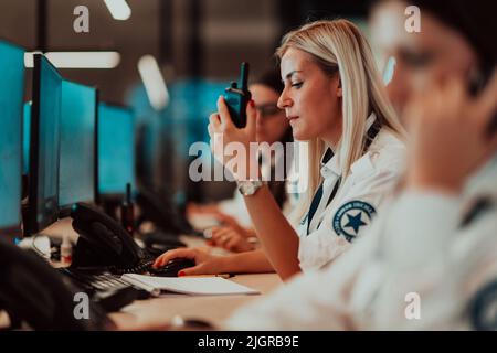 Opérateur de sécurité féminin tenant la radio portable en main tout en travaillant dans un système de données bureaux de la salle de contrôle opérateur technique travaillant à la station de travail Banque D'Images