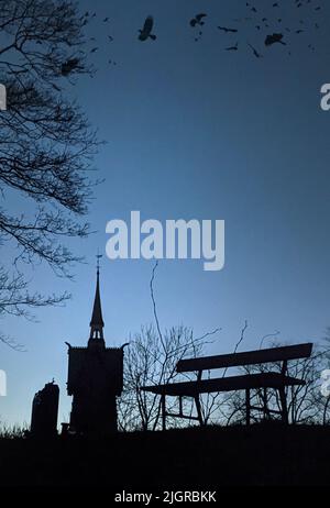 Une vue effrayante d'une église dans un cimetière avec des oiseaux dans le ciel et un banc devant le concept d'Halloween Banque D'Images